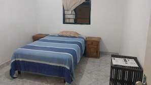 Un dormitorio con cama, dos mesitas de noche, una ventana con cortina y un pequeño armario de madera.