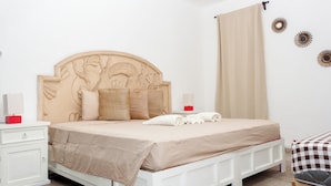 Une chambre à coucher avec un lit blanc, une literie beige, une table de chevet avec une lampe et une tête de lit en bois.