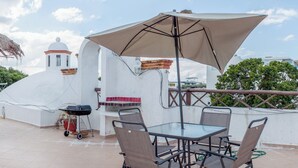 Une terrasse sur le toit, avec une table et des chaises, un barbecue et un grand parasol.