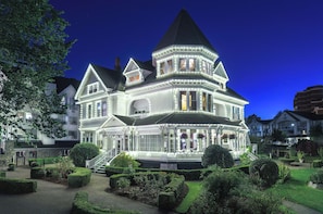 A large, ornate Victorian-style building with multiple stories, a prominent turret, and a well-maintained garden.