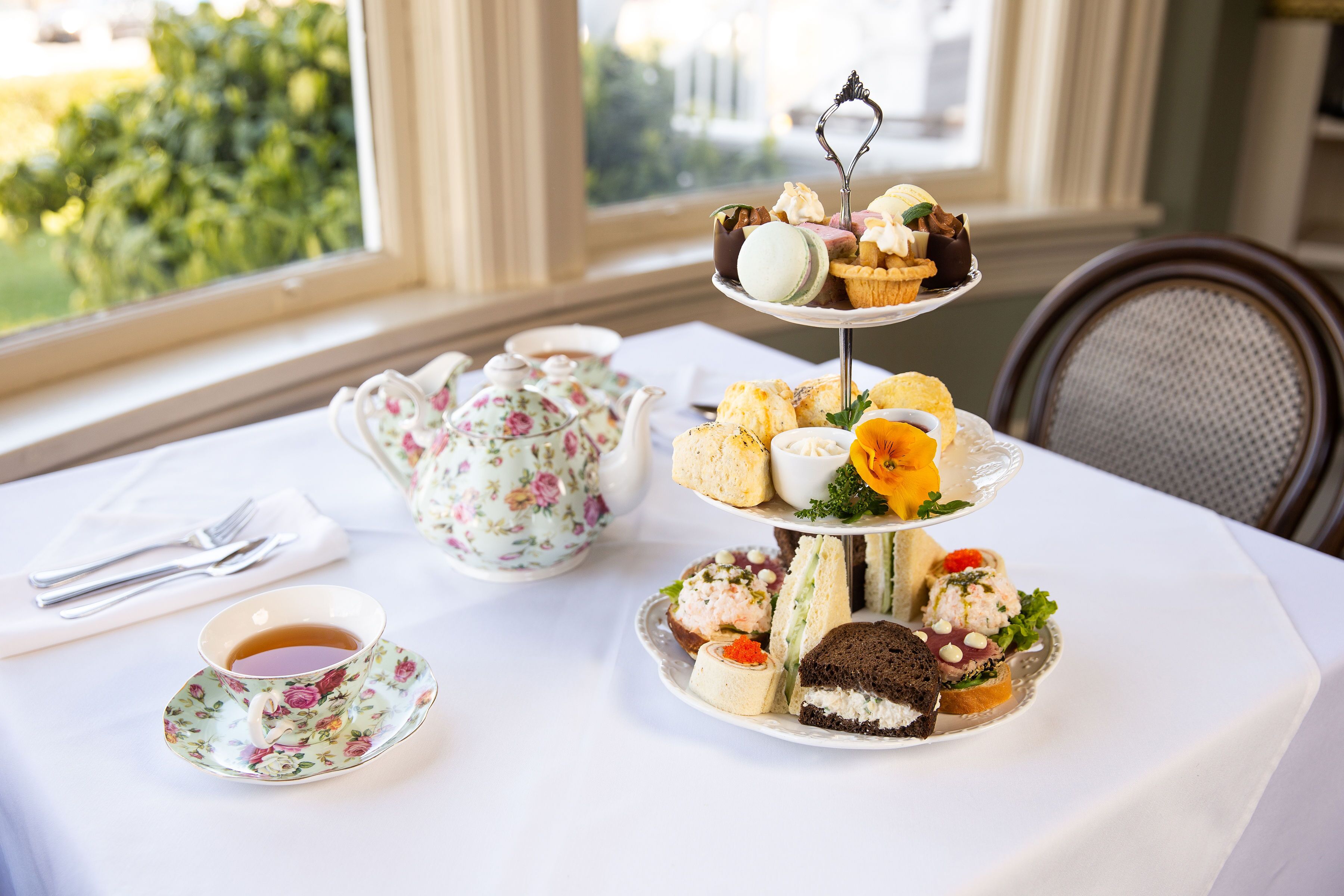 A three-tiered dessert stand with various pastries and sandwiches on a white tablecloth.