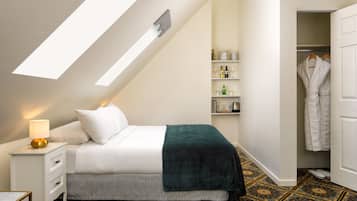 A bedroom with a skylight, a bed with a green throw, a bedside table with a lamp, and a patterned floor.
