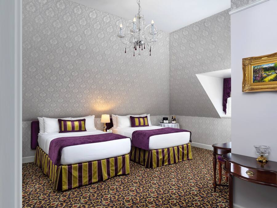 A hotel room with two beds, a chandelier, a small table with a lamp, and a decorative mirror.