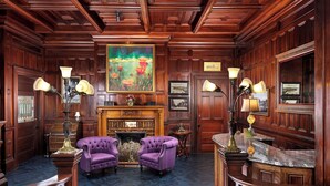 A formal room with wooden paneling, a fireplace, two purple armchairs, and a large painting above the fireplace. - Pendray Inn & Tea House (Victoria)