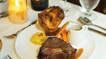Une assiette contenant un steak, des Yorkshire puddings et des légumes, accompagnée de verres à vin et d’une bougie.