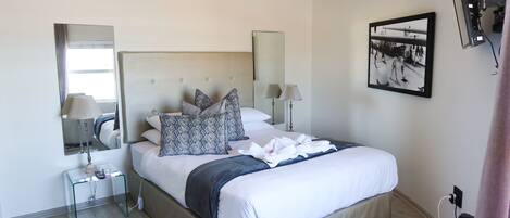 A modern hotel room with a large bed, bedside tables, a mirror, and a framed photograph on the wall.