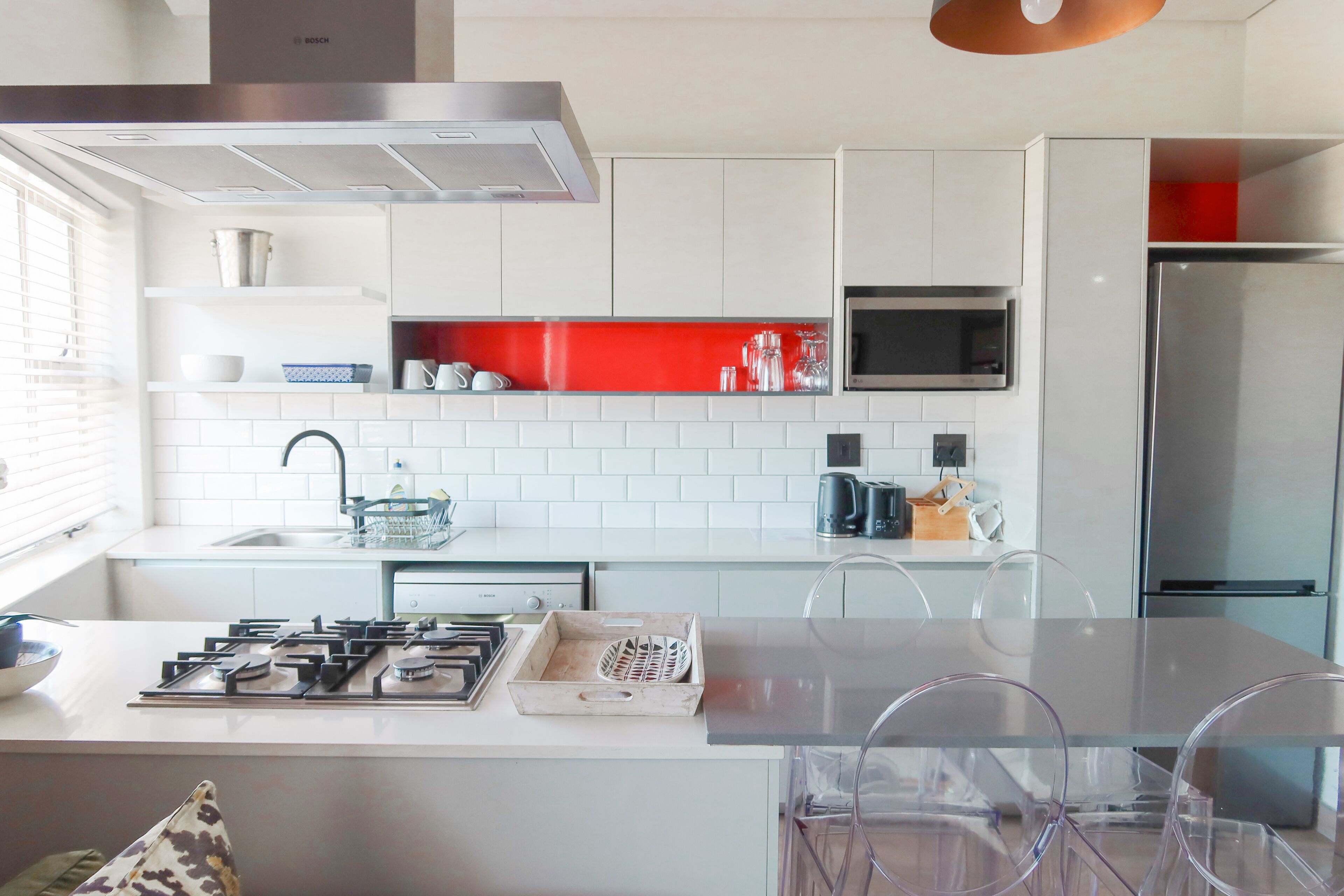 A modern kitchen with white cabinets, a red backsplash, stainless steel appliances, and a glass island with chairs.