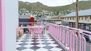 A balcony with a checkered floor, pink chairs, and a view of a town with buildings and a hill in the background. - 55 on Main Guesthouse and Spa (Cape Town)