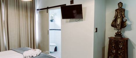A hotel room with a bed, a television, a statue, and a bathroom visible through a door.