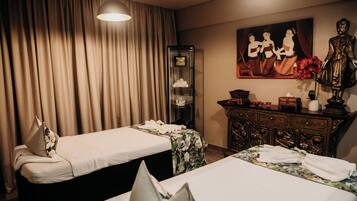 Two single beds with neatly folded linens and pillows, a traditional dresser with mirror and shelf, and a painting adorn the room.