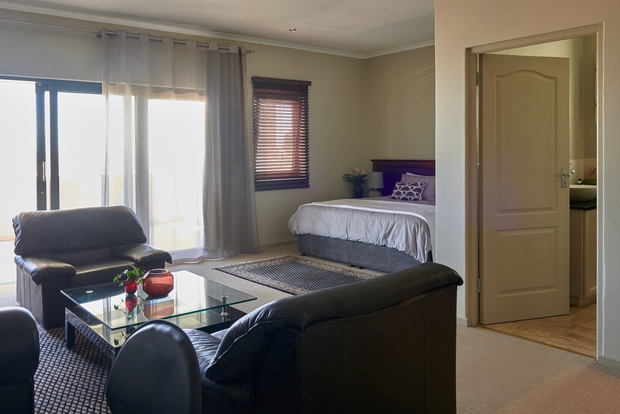 Une chambre d’hôtel avec un lit, un canapé, une table basse en verre et une porte donnant sur une autre pièce.
