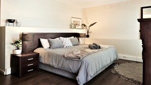 Un dormitorio con una cama, mesitas de noche, una lámpara, un espejo, una planta y un cuadro en la pared.