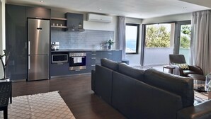 Una cocina moderna con horno y microondas integrados, un sofá gris y vistas al exterior a través de grandes ventanales.