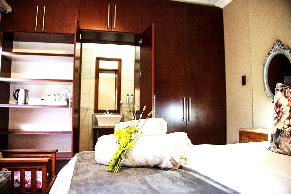 A hotel room with a bed, a nightstand, a wooden chair, a wardrobe, a mirror, and a bathroom visible through an open door.