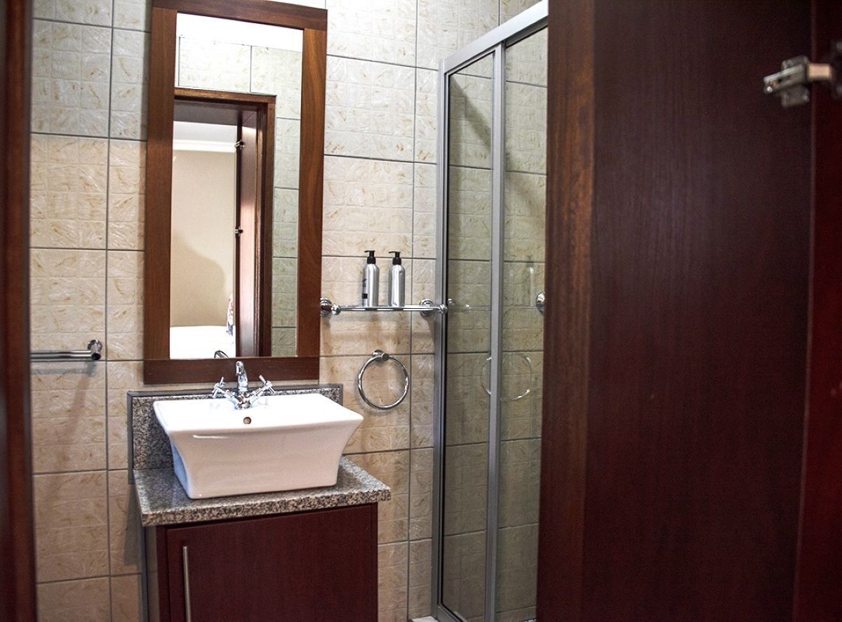 A bathroom with a white sink, a mirror, and a glass shower door.
