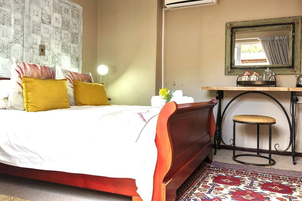 A bedroom with a bed, bedside table, mirror, and a small stool.