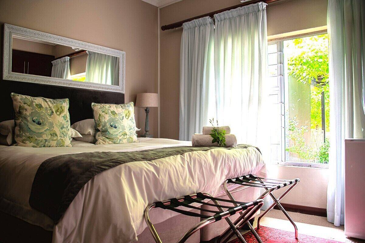 A bedroom with a bed, a mirror, a window with curtains, and a view of greenery outside.