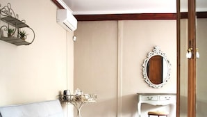 A bedroom with a grey sofa, a white vanity with a mirror, a small table with decorative items, and a white rug. - Kroon Manor (Moqhaka)
