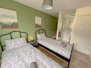 A bedroom with two beds, a nightstand with a lamp, a shower, and a door. - Horizon Apartments (Southampton)