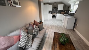 A modern living room with a grey sofa, patterned cushions, a wooden coffee table, and a hanging pendant light. - Horizon Apartments (Southampton)