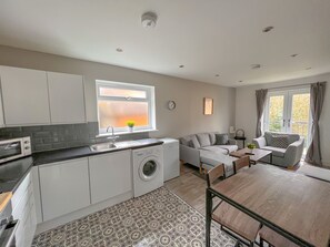 A modern kitchen with a washing machine, a dining area with a table and chairs, and a living area with a sofa and a window with curtains. - Horizon Apartments (Southampton)