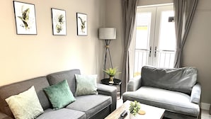 A modern living room with two grey sofas, a wooden coffee table, and a floor lamp. There are three framed botanical prints on the wall. - Horizon Apartments (Southampton)