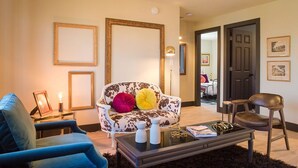 Un salon comprenant un canapé, un fauteuil bleu, une table basse et une porte donnant sur une autre pièce.