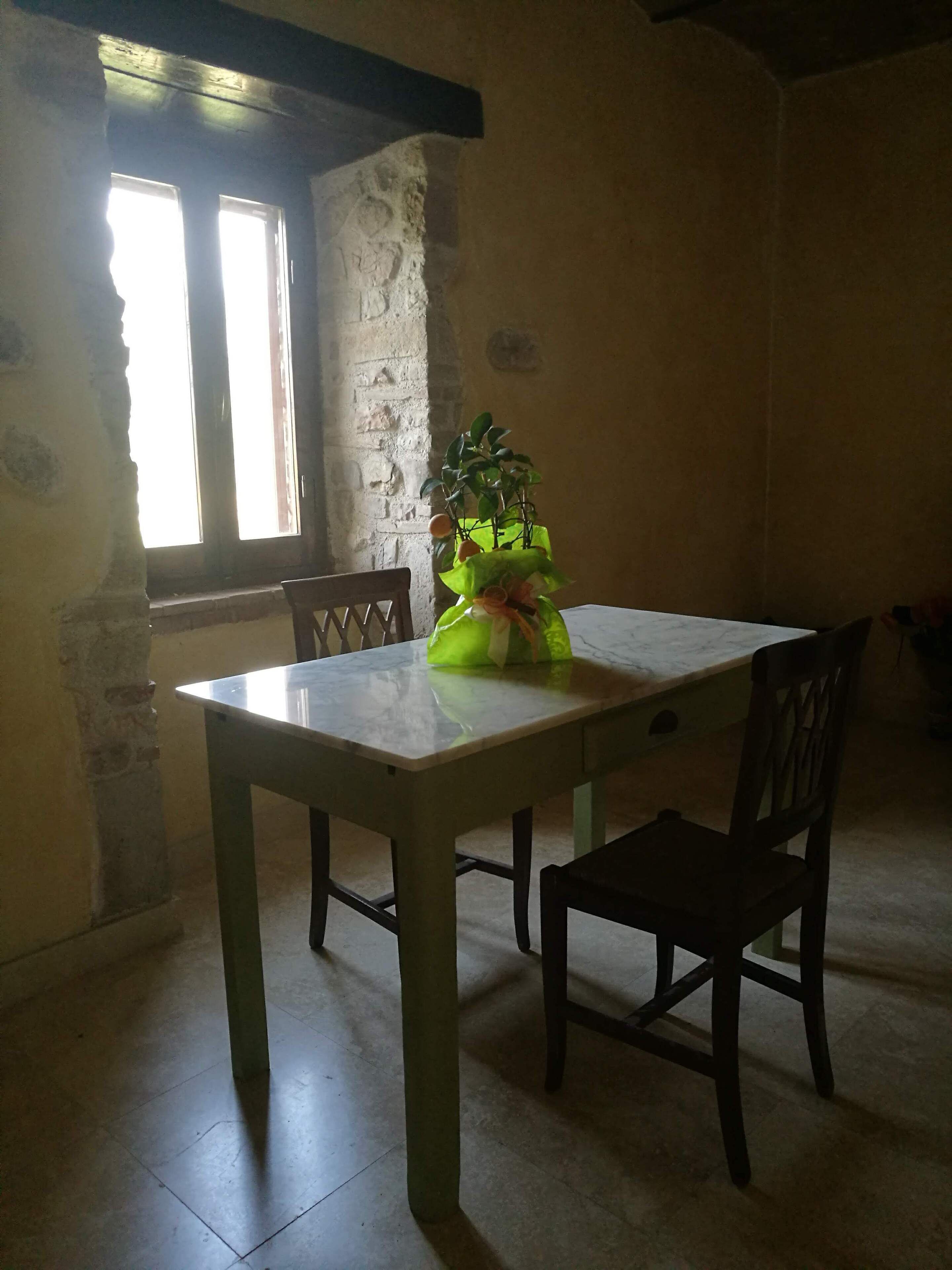 Ein Essbereich mit einem Marmortisch, zwei Holzstühlen, einem Blumentopf und einem Fenster mit Tageslicht.