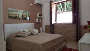 Una camera da letto con un letto, un quadro, una finestra con tende, un comodino e una piccola mensola con oggetti decorativi.
