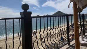 Blick auf einen Strand mit einer Geländer, Liegestühlen und Sonnenschirmen.
