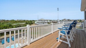 Terraza de madera con barandillas blancas, una piscina y sillas azules.