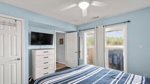 Un dormitorio con cama, televisor, cómoda y ventilador de techo.