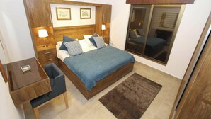 Ein Schlafzimmer mit Bett, Nachttischen, Schreibtisch, Teppich und einem Fenster mit Jalousien.