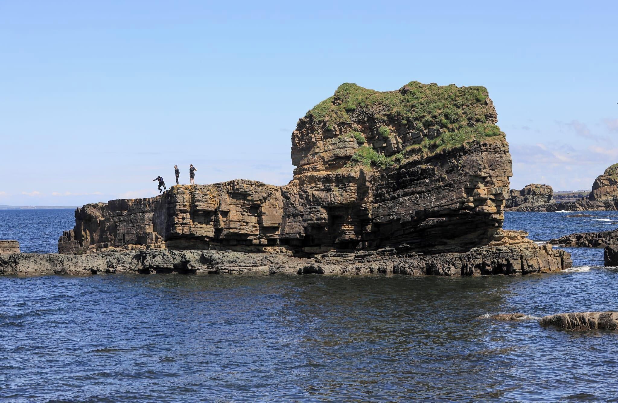 A rocky coastal landscape with three people standing on a cliff.
