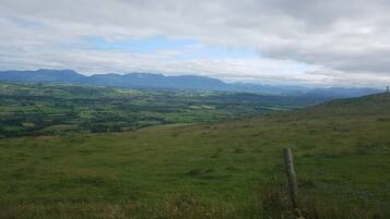 A panoramic view of a hilly landscape with fields and distant mountains.