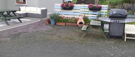A patio with a grill, a bench, and potted plants.
