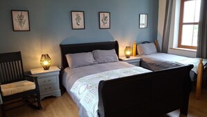 Ein Schlafzimmer mit zwei Betten, Nachttischlampen, einem Sessel und gerahmten Pflanzenbildern an der Wand.