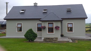 Ein zweistöckiges Haus mit grauem Dach, weißer Fassade und einem kleinen Vorgarten.
