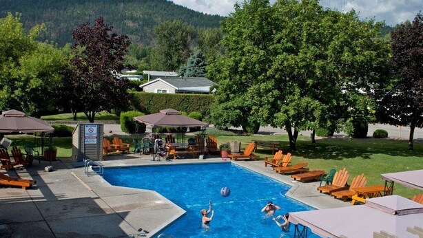 A swimming pool with lounge chairs and umbrellas, surrounded by trees and a mountain backdrop. - Kelowna Timeshare July Rental for 1 Week (Kelowna)
