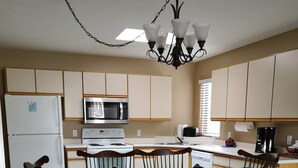 A compact kitchen with a dining table and chairs, a refrigerator, microwave, stove, and a chandelier. - Kelowna Timeshare July Rental for 1 Week (Kelowna)