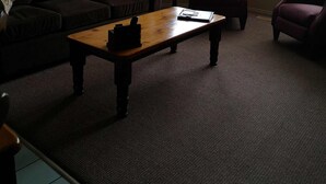 A living room with a brown sofa, a wooden coffee table, and a red armchair. There is a framed picture on the wall and a window with blinds. - Kelowna Timeshare July Rental for 1 Week (Kelowna)
