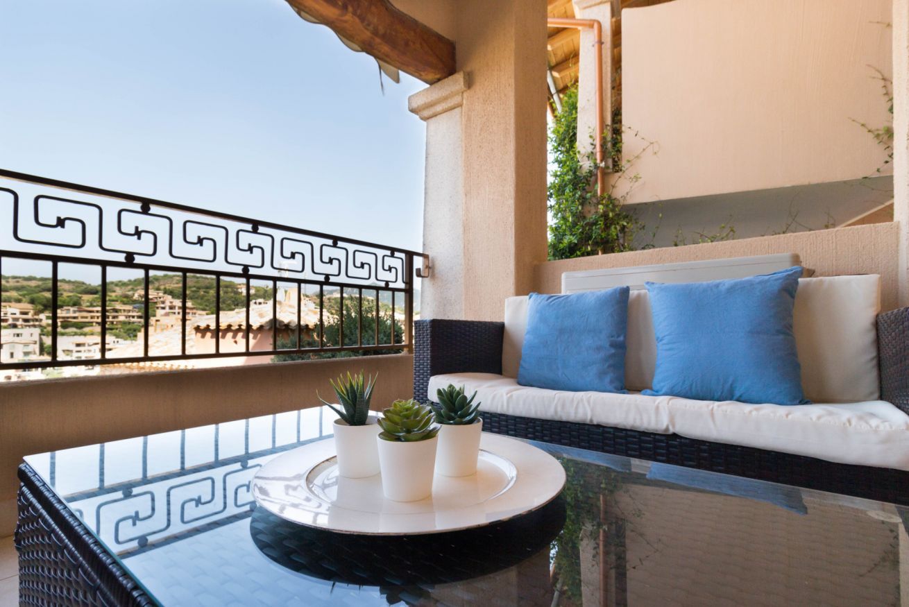 A balcony with a wicker sofa, blue cushions, and potted plants.