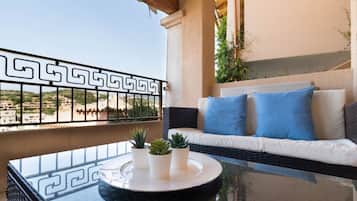 A balcony with a wicker sofa, blue cushions, and potted plants.