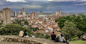 Vista panorâmica de uma paisagem urbana com edifícios históricos e arranha-céus modernos, vista de uma muralha de pedra onde pessoas sentam e ficam em pé.