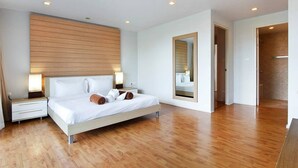 Une chambre d’hôtel moderne avec une tête de lit en bois, un grand miroir, un lit recouvert de draps blancs et un plancher en bois.