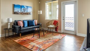 A living room with a black leather sofa, a colorful rug, a cactus, and a window with blinds. - Sandia Peak Apartments by Frontdesk (Albuquerque)