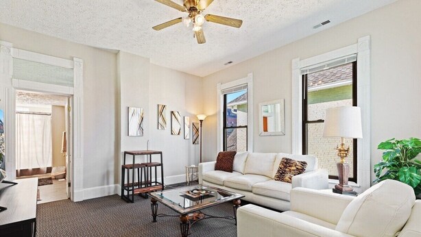 A living room with a white sofa, a glass coffee table, a ceiling fan, and artwork on the walls. - Indy Stadium Villas 707 (Indianapolis)