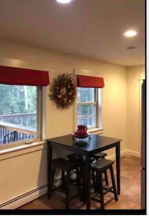 Enjoy meals in this cozy dining area with a table and two chairs, a decorative wreath, and natural light pouring in through the windows.