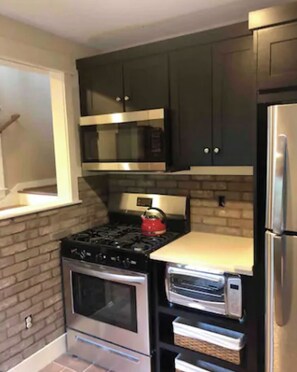 Modern kitchen with stainless steel appliances, dark cabinetry, and a brick backsplash.