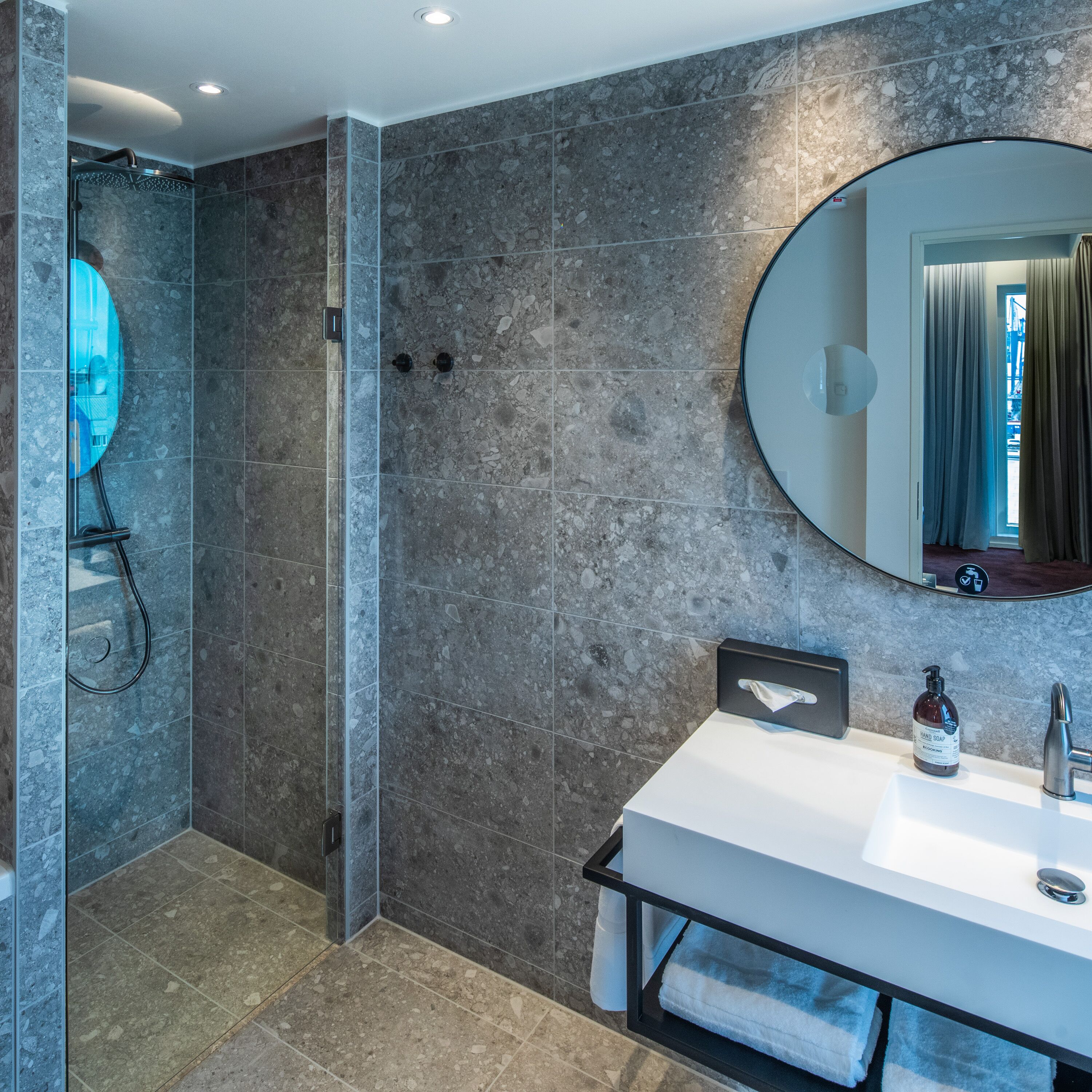 A modern bathroom with a glass-enclosed shower, a large mirror, and a white sink with a towel rack.